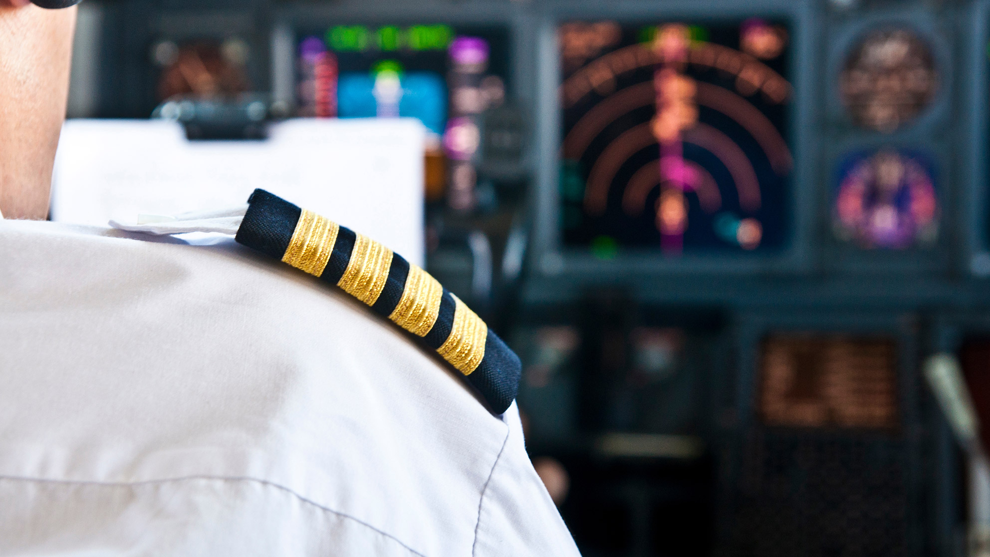 The shoulder of an airplane pilot in front of radar equipment