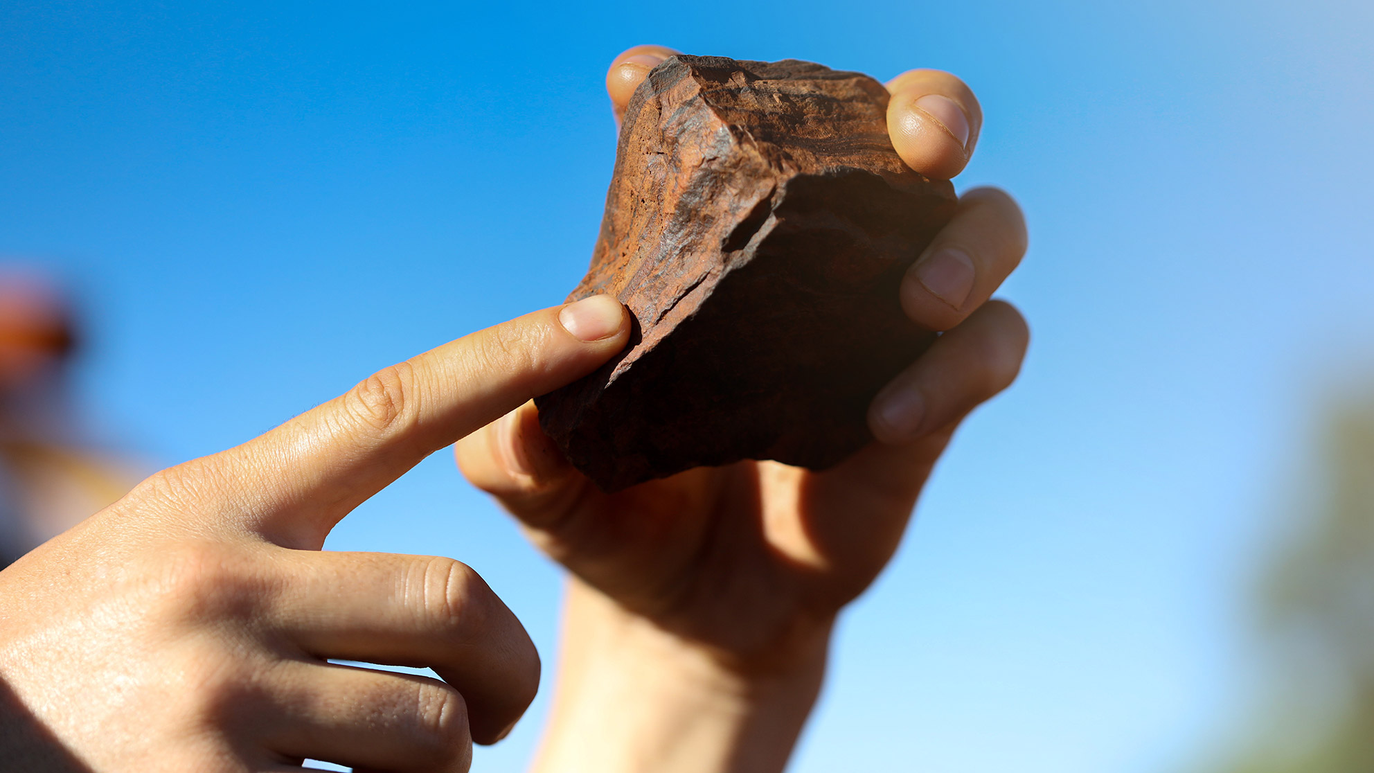 A red-brown stone held in a pair of hands in front of a blue sky