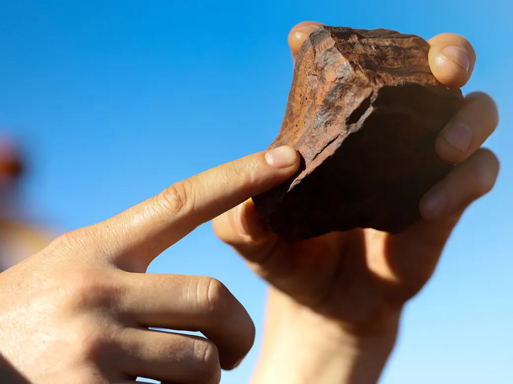 A red-brown stone held in a pair of hands in front of a blue sky