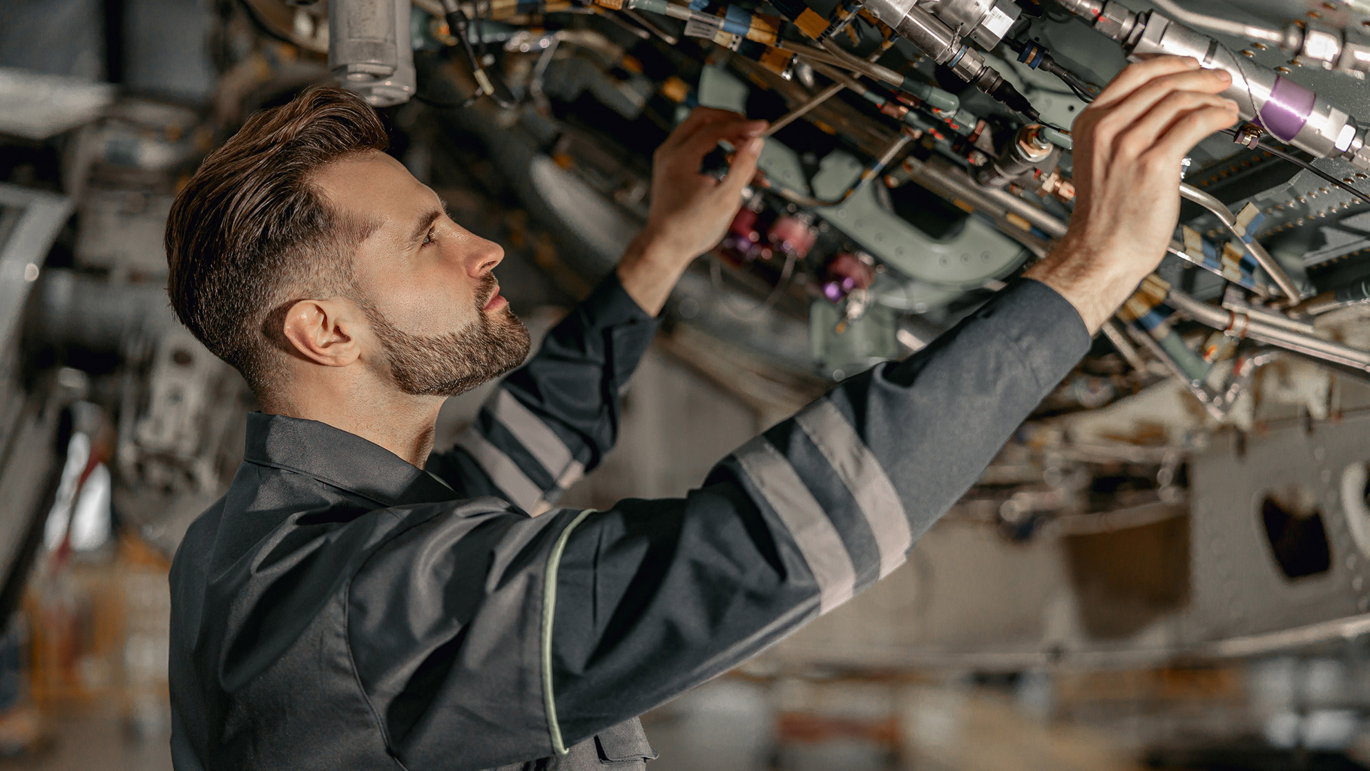 younger mechanic in work clothes checks mechanical airplane components 