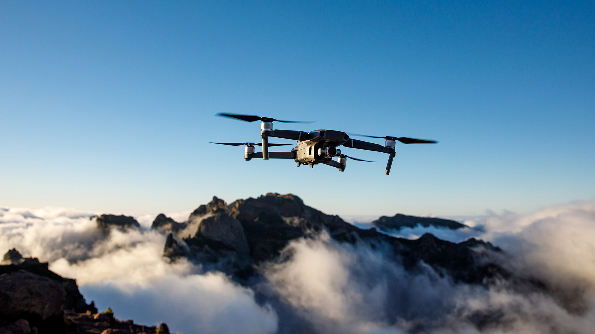 A drone flies above the cloud line in the mountains against a blue sky