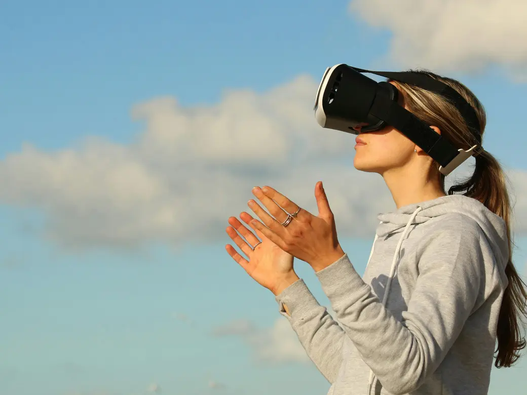 Woman in front of sky with seagull in the background, wearing VR glasses and spreading out her hands