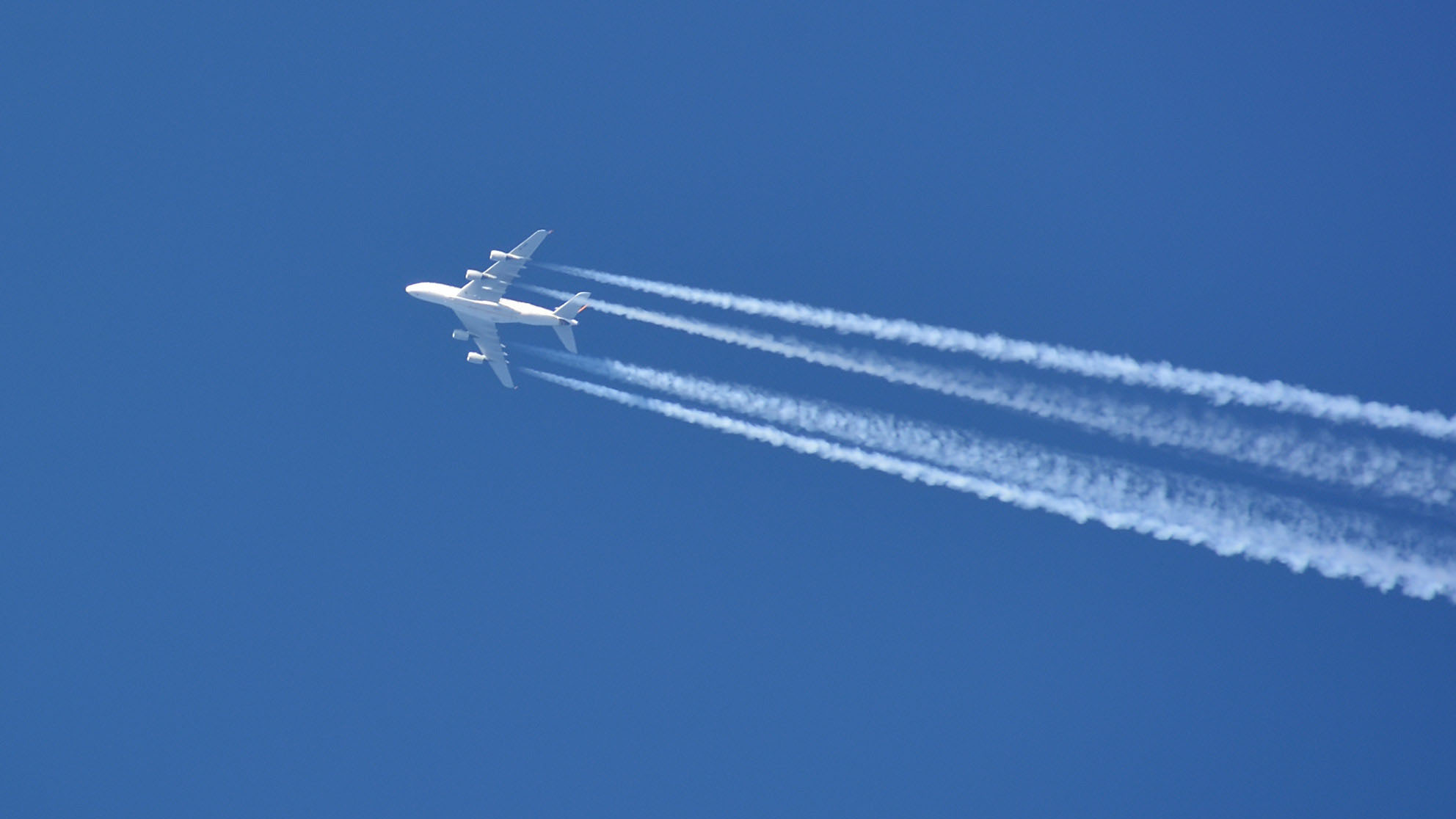 White airplane with condense stripes from below in front of a blue sky 