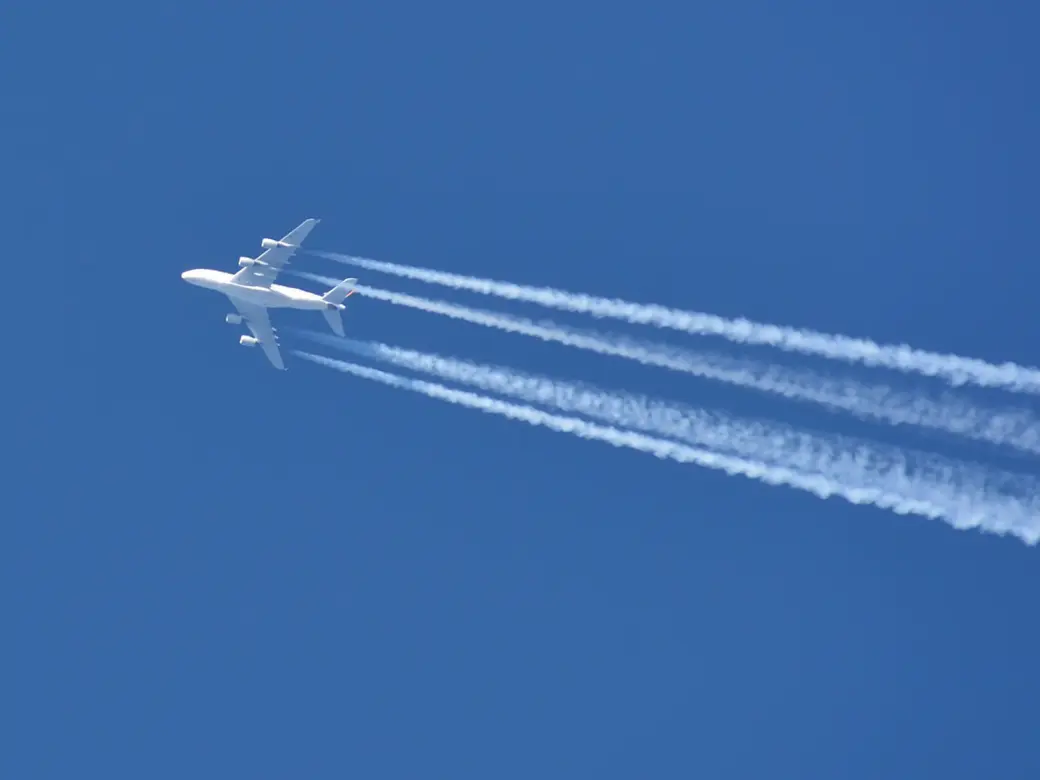 White airplane with condense stripes from below in front of a blue sky 