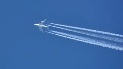 White airplane with condense stripes from below in front of a blue sky
