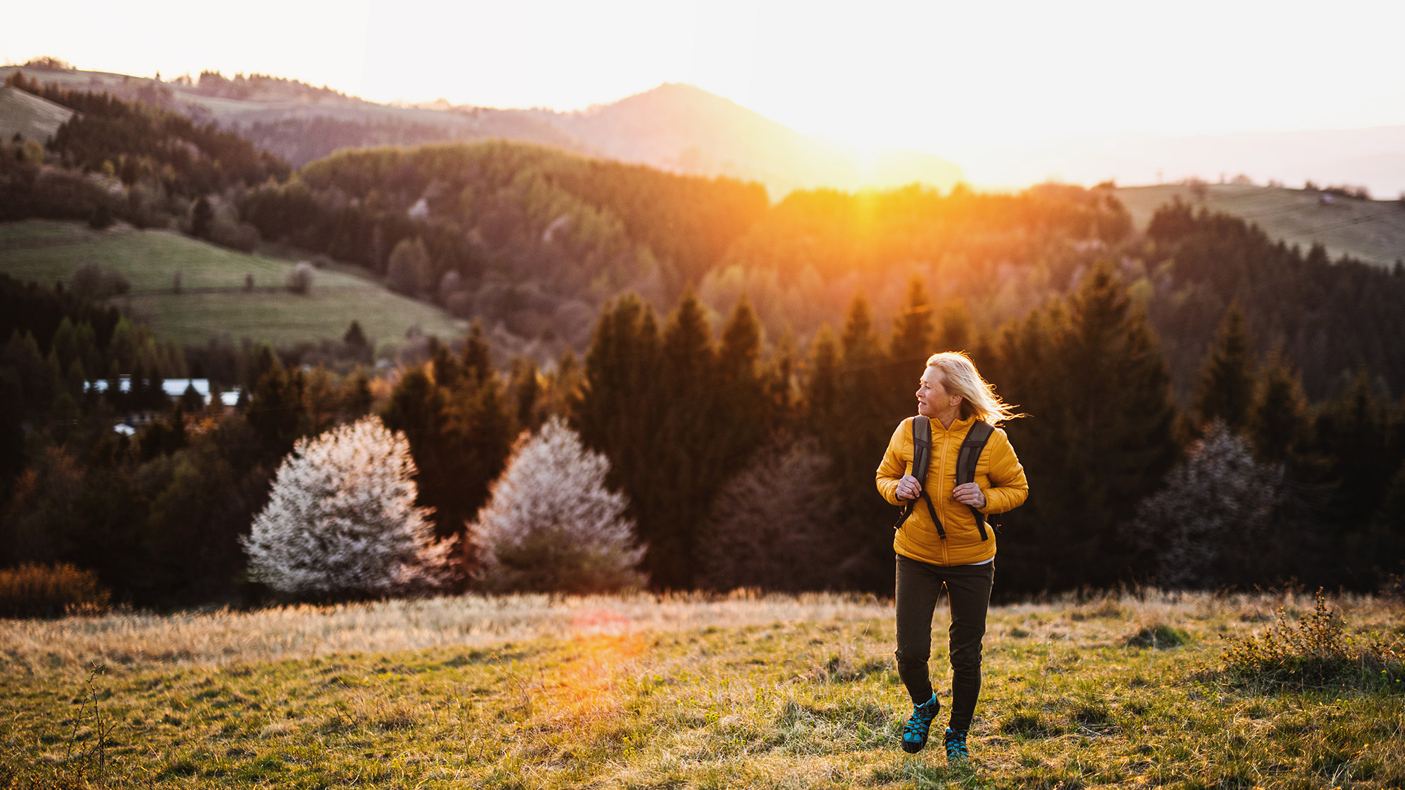 Woman hiking in the mountains on a green meadow at sunset