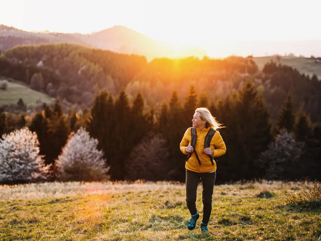 Woman hiking in the mountains on a green meadow at sunset